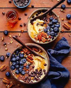 two bowls filled with granola, blueberries and pecans on top of a wooden table