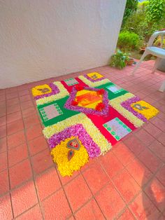 a colorful rug is on the ground near a white chair and some flowers in front of it