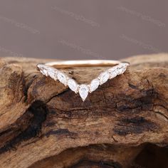 a white gold wedding band with three pear shaped diamonds on it, sitting on top of a piece of wood