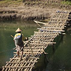 a man standing on top of a wooden bridge made out of bamboo rafts in the water