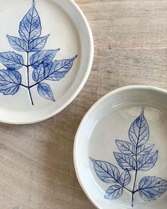 two bowls with leaves painted on them sitting on top of a wooden table next to each other