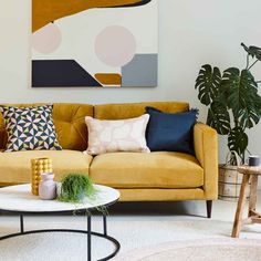 a living room with yellow couches and colorful pillows on the table in front of it