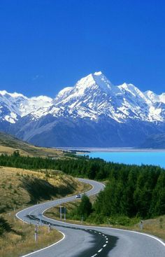 an empty road with mountains in the background and snow on the top of the mountain