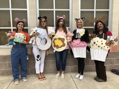 four girls in costumes holding up signs and cupcakes on their faces while standing next to each other