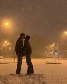 two people standing in the snow at night with their heads touching each other's noses