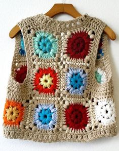 a crocheted sweater hanging on a wooden hanger next to a white wall