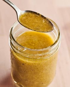 a spoon full of liquid sitting on top of a jar filled with something orange and yellow