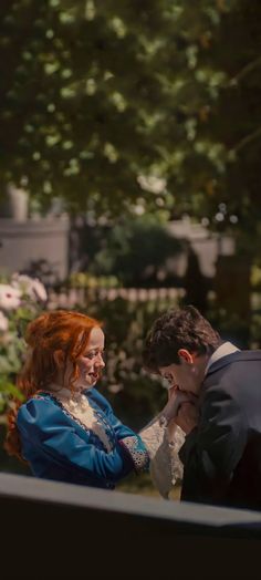 a man and woman standing next to each other in front of some flowers on a porch