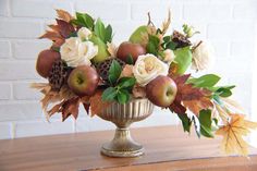 a vase filled with apples and flowers on top of a wooden table