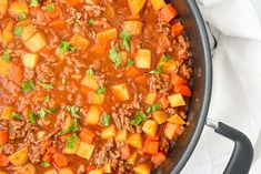 a pot filled with stew and vegetables on top of a white cloth next to a spoon