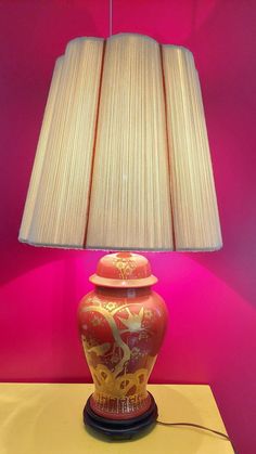 a lamp that is sitting on top of a table next to a red vase with gold designs