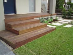 a wooden deck in front of a house with grass on the ground and steps leading up to it