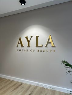 the logo for a house of beauty in gold letters on a white wall next to a potted plant