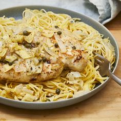 a pan filled with chicken and noodles on top of a wooden table next to a fork