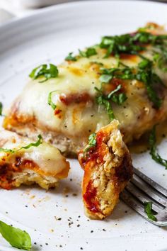 a white plate topped with meat covered in cheese and sauces next to a fork