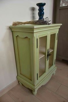 a green cabinet sitting in the corner of a room with a vase on top of it