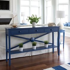 a blue console table with three potted plants on it and a white couch in the background