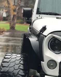 the front end of a white jeep parked on top of a wet parking lot next to a tree