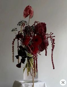 a vase filled with red flowers on top of a white table cloth covered tablecloth