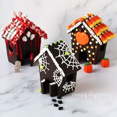 three halloween houses made out of candy sticks on a marble countertop with white and black speckles