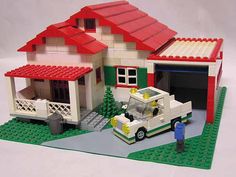 a lego model of a house with a fire truck parked in front of it and a man standing next to it