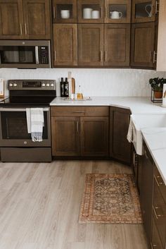 a kitchen with wooden cabinets and white counter tops, an area rug on the floor