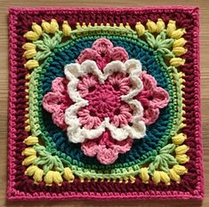 a crocheted square with a flower in the center on a wooden table top