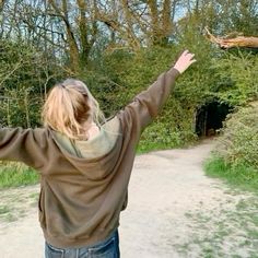 a woman is standing on a dirt path with her arms outstretched