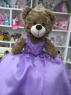 a brown teddy bear wearing a purple dress in a room full of dolls and toys