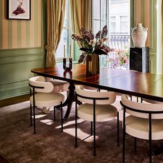 a dining room table with four chairs and a vase on the wall next to it