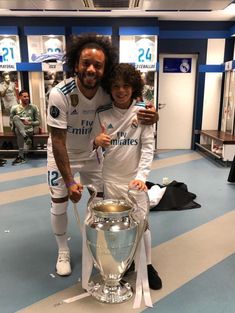 a man standing next to a woman in front of a soccer trophy on a blue and white floor