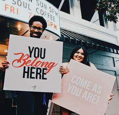 two people holding signs that say you belong here and come as you are on the street