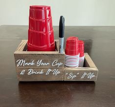 a wooden box with red cups and pens in it