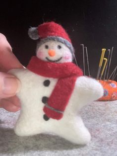 a hand holding a snowman ornament with pins in it