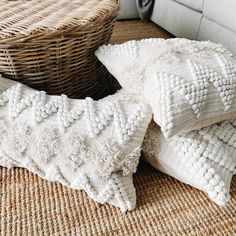 three white pillows sitting on top of a floor next to a wicker basket and pillow