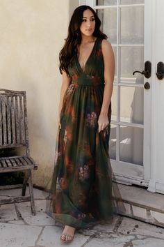 a woman standing in front of a door wearing a long dress with flowers on it