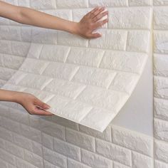 two hands reaching for a piece of white paper on a brick wall that is being held by another hand