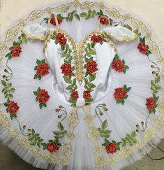 a white dress with red flowers and green leaves on the skirt is displayed in front of a wall