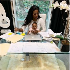 a woman sitting at a desk with a baby in her lap and papers on the table