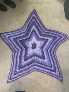 a purple crocheted star is laying on the floor next to someone's shoes