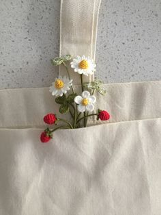 flowers are in the pocket of a white tote bag hanging from a hook on a wall