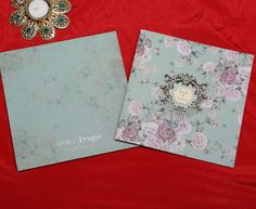 two wedding cards on a red cloth next to a candle and broochel decoration