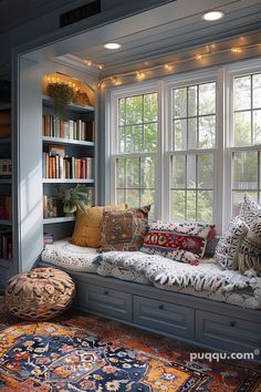 a window seat with many pillows on it in front of a bookshelf filled with books