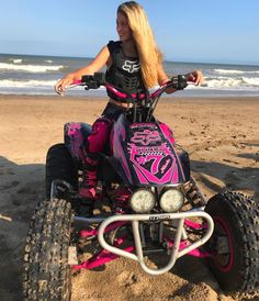 a woman riding on the back of a pink four - wheeler down a sandy beach