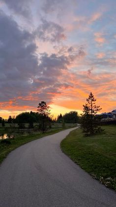 the sun is setting behind some trees and clouds in the sky over a path that leads to a pond