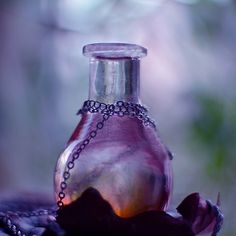 a glass bottle with a chain around it sitting on a table next to a flower