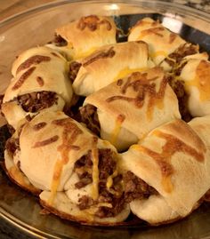 a glass plate topped with cheeseburger rolls covered in melted cheese and chili sauce