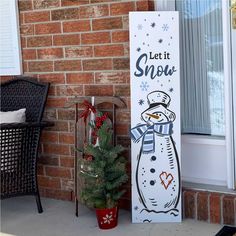 a snowman standing next to a christmas tree in front of a brick wall with the words let it snow written on it