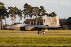 a fighter jet taking off from an airport runway with trees in the backgroud