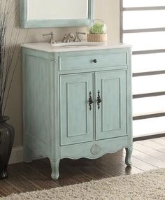 a bathroom vanity with a white marble top and blue painted wood cabinet, along with a black vase filled with flowers